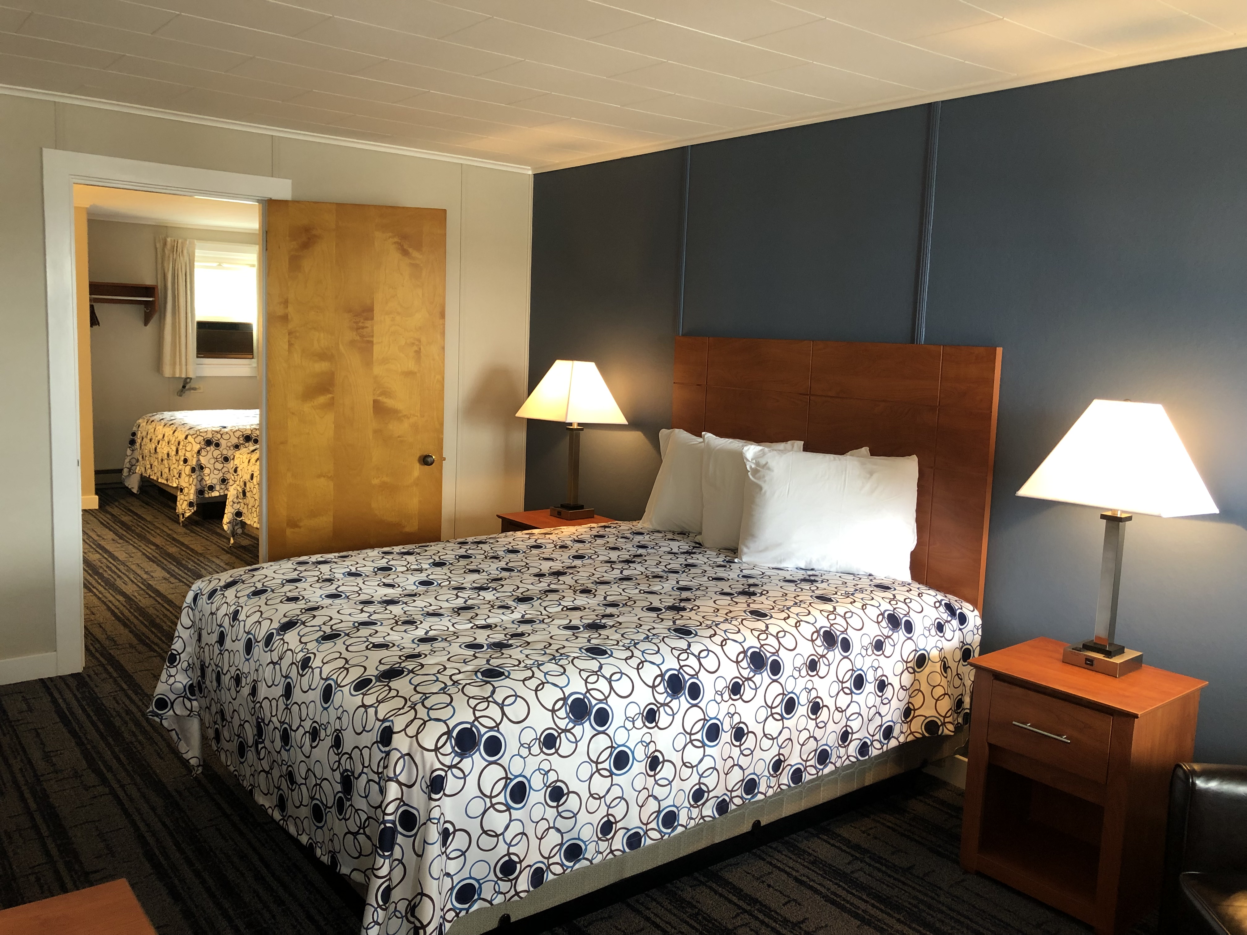 A hotel room with a bed, two nightstands, and a doorway leading to another room.